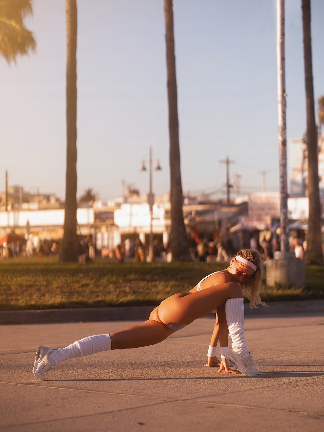 Katerina in a lunge position on the pavement at Venice Beach with palm trees and boardwalk shops behind her