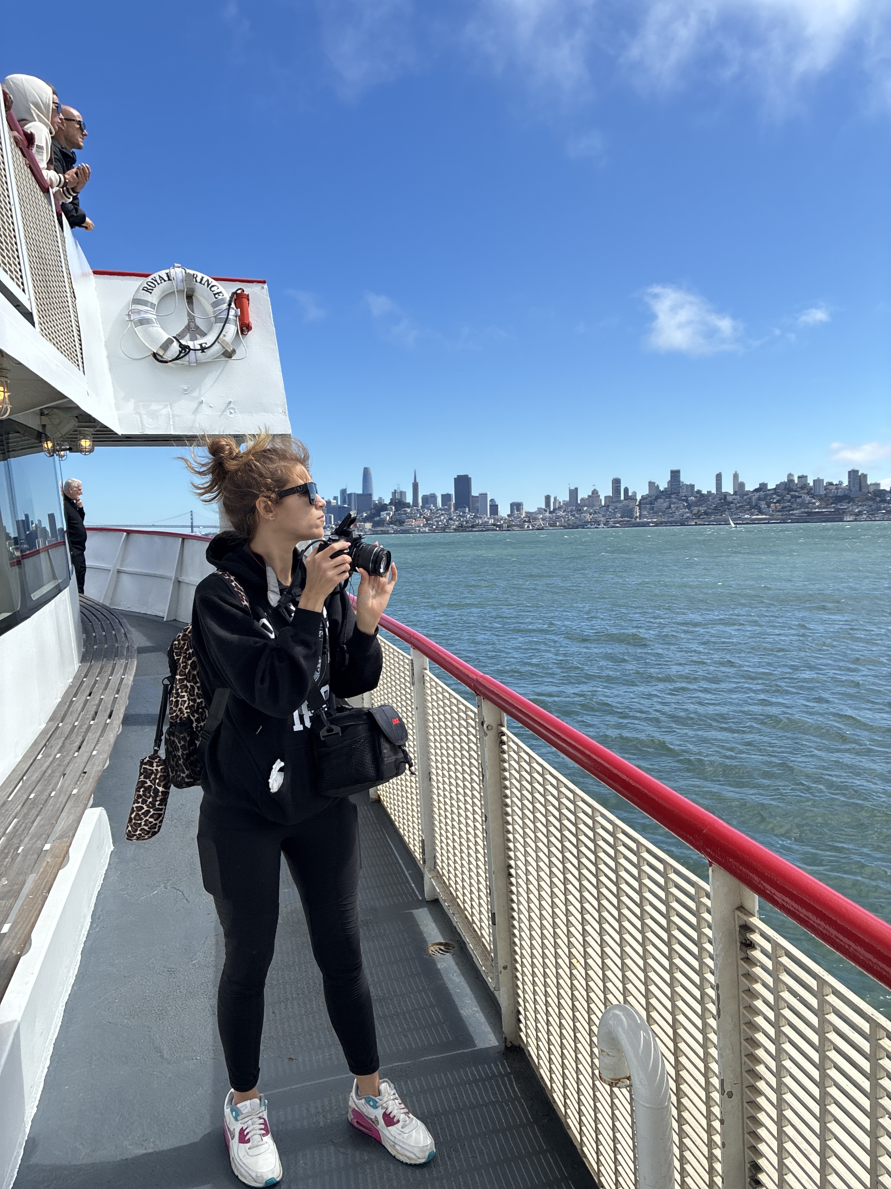 Princess Cat on the San Francisco Alcatraz tour boat, camera raised, skyline across the bay