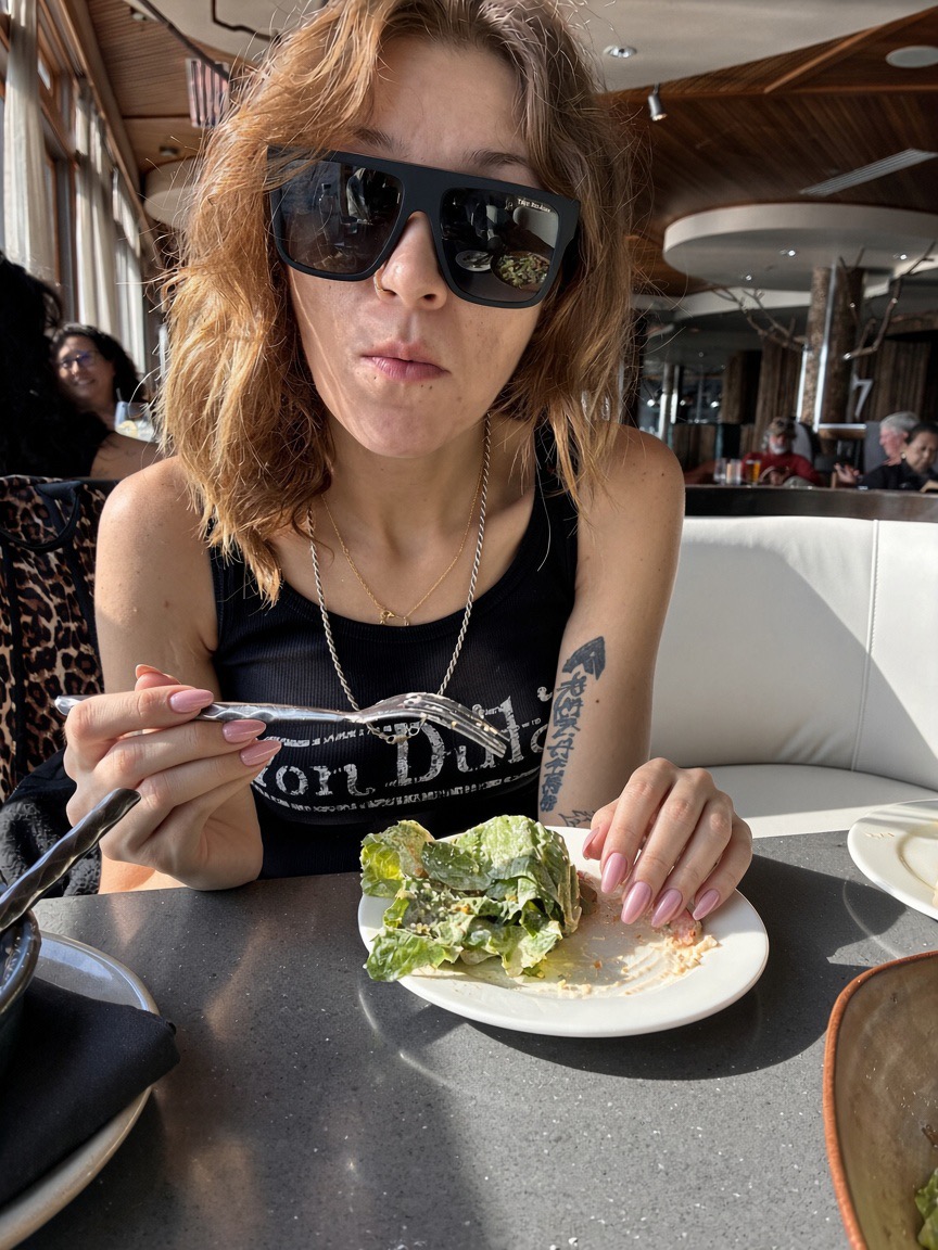 Siarra Cat in sunglasses in a white booth holding a fork over a mostly finished Caesar plate at Six Seven
