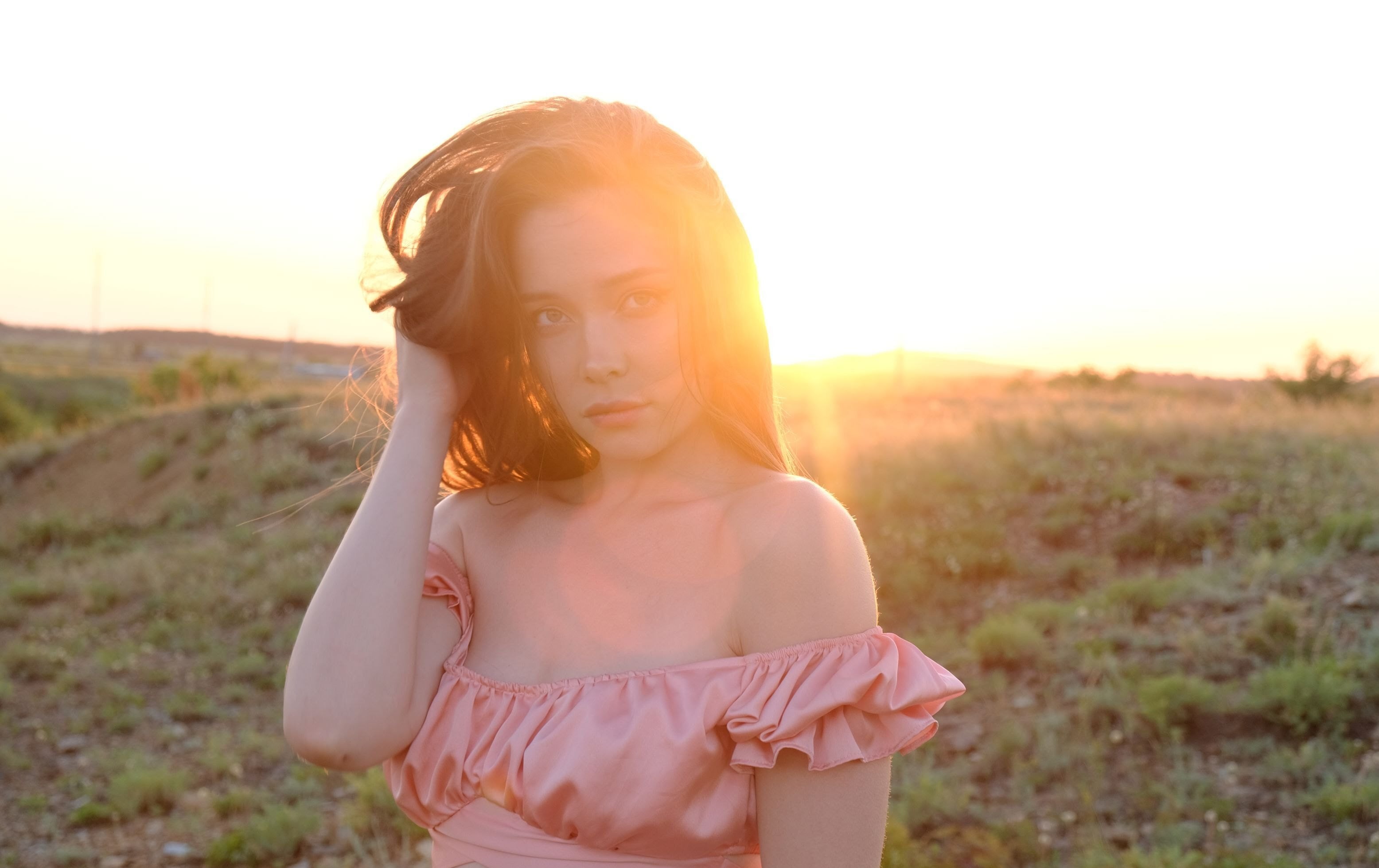 Kate Cat in a peach satin off-the-shoulder top, eyes closed, hair catching the wind against a clear blue Kansas sky